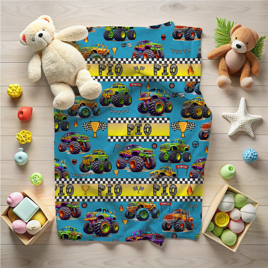 Children's blanket with monster truck design on a wooden floor with toys around
