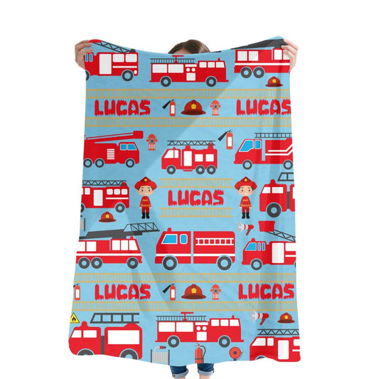 Person holding a blanket with fire truck and firefighter designs, featuring the name 'Lucas'.