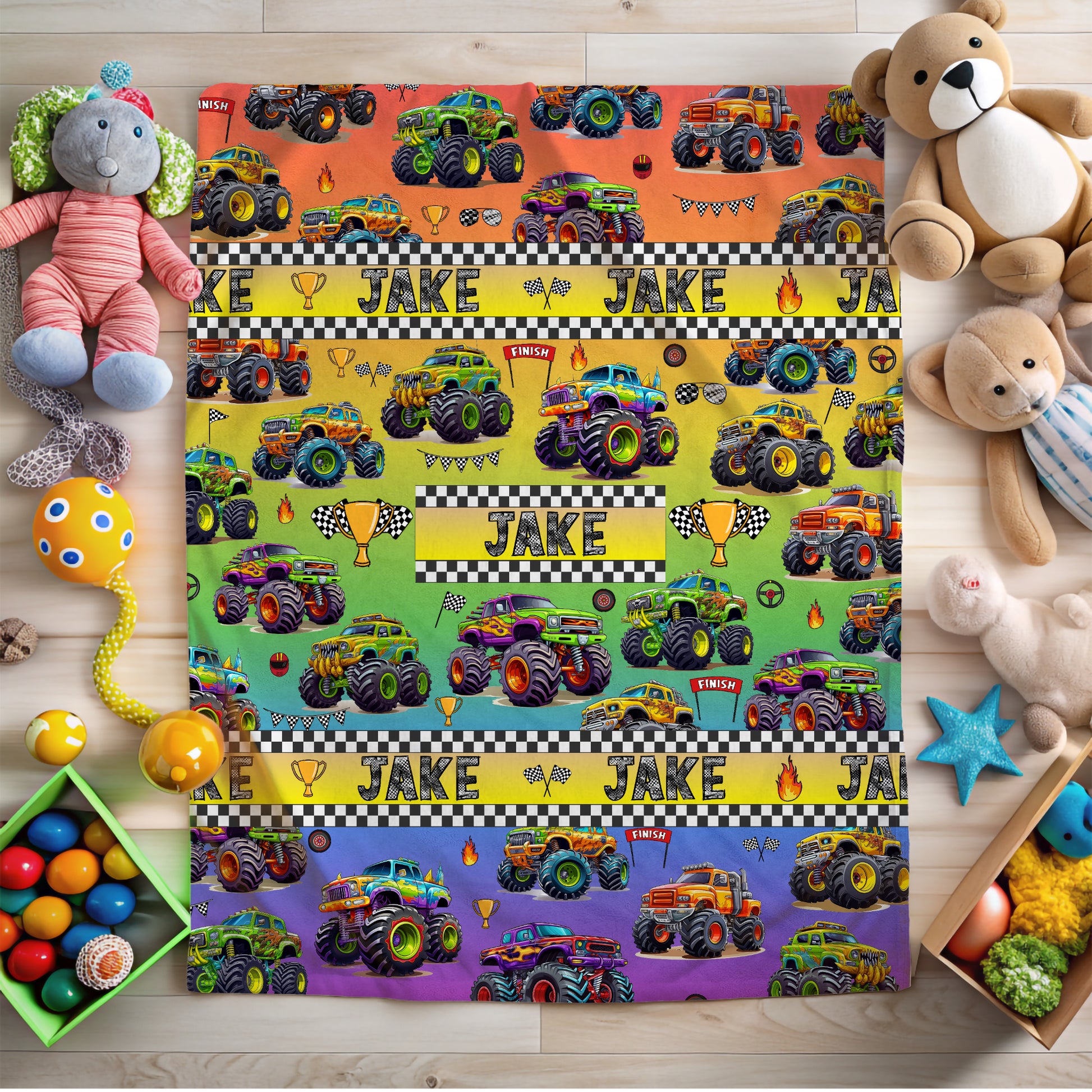 Personalized blanket with monster truck pattern and name 'Jake', surrounded by toys on a wooden surface.